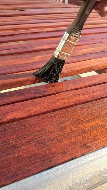 paint brush brushing a piece of cherry colored wood