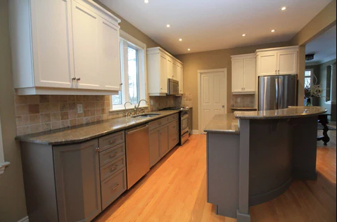 kitchen with white upper cabinets, grey lower cabinets, wood flooring and an island in the middle 